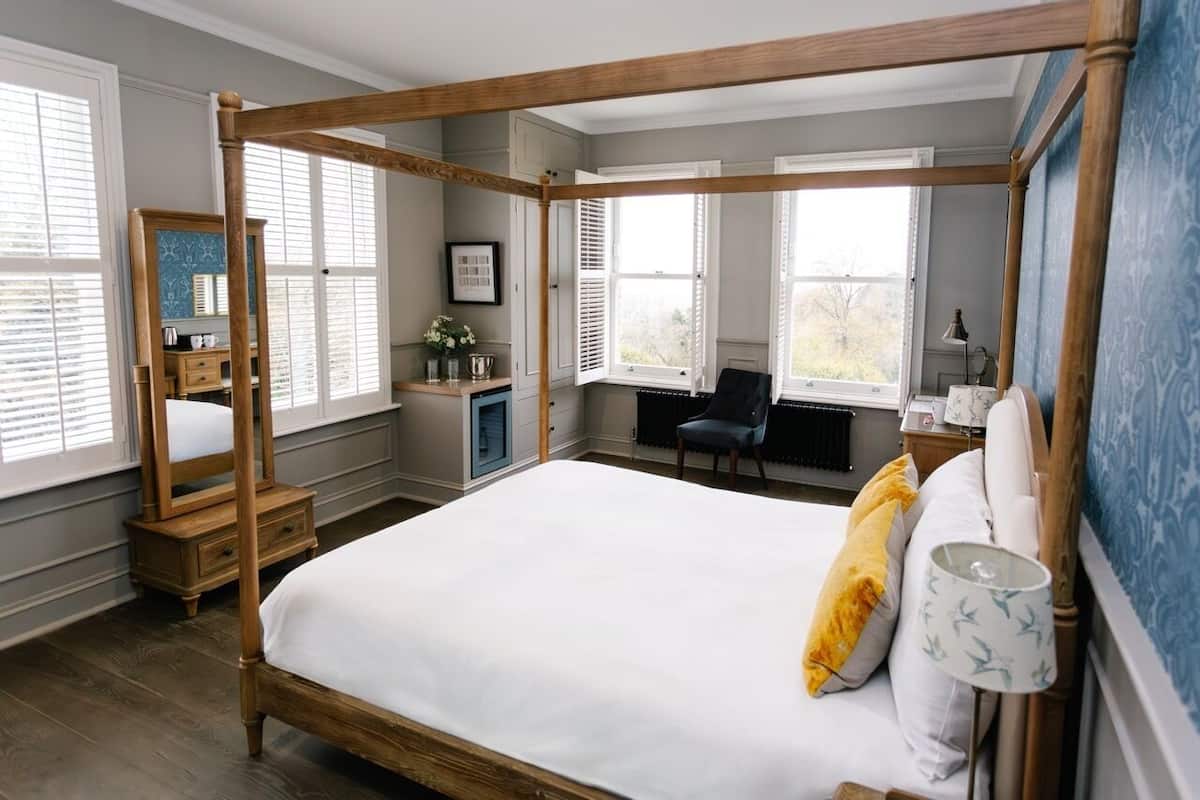 A four-poster bed with a wooden frame, a bedside table, a chair, and a window with shutters.