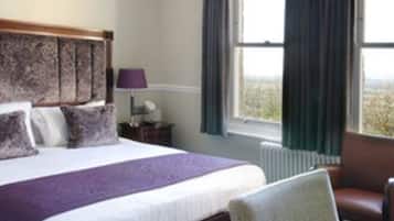 A hotel room with a large bed, a chair, a nightstand, and a window with curtains.
