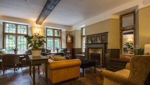 A cozy living room with a fireplace, wooden flooring, and large windows. - Hatton Court (Gloucester)