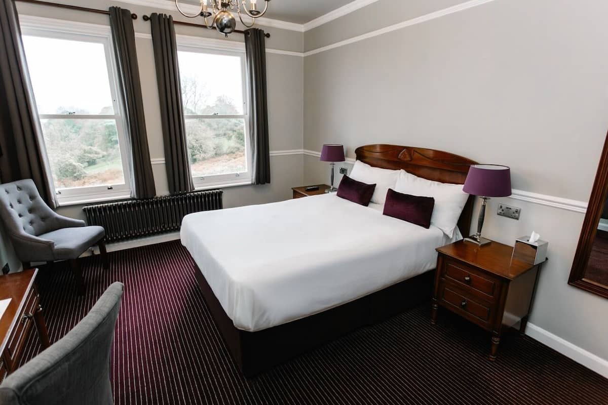 A hotel room with a large bed, two bedside tables, a chair, a radiator, and a window with curtains.