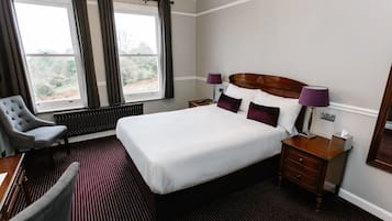 A hotel room with a large bed, two bedside tables, a chair, a radiator, and a window with curtains.