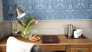 A wooden desk with a lamp, a vase with flowers, a plate with pastries, a book, a coffee pot, and a cup. - Hatton Court (Gloucester)