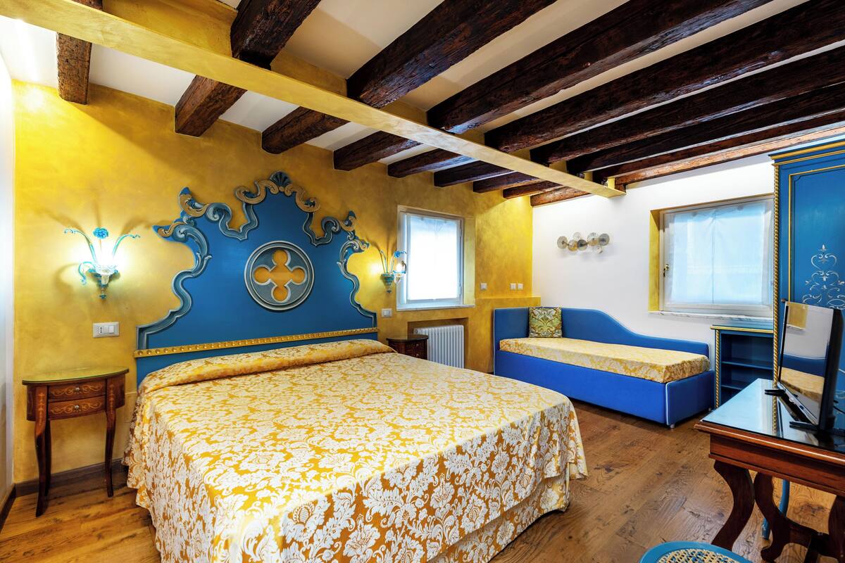 A bedroom with a bed, a blue sofa, a wooden table, and a window.