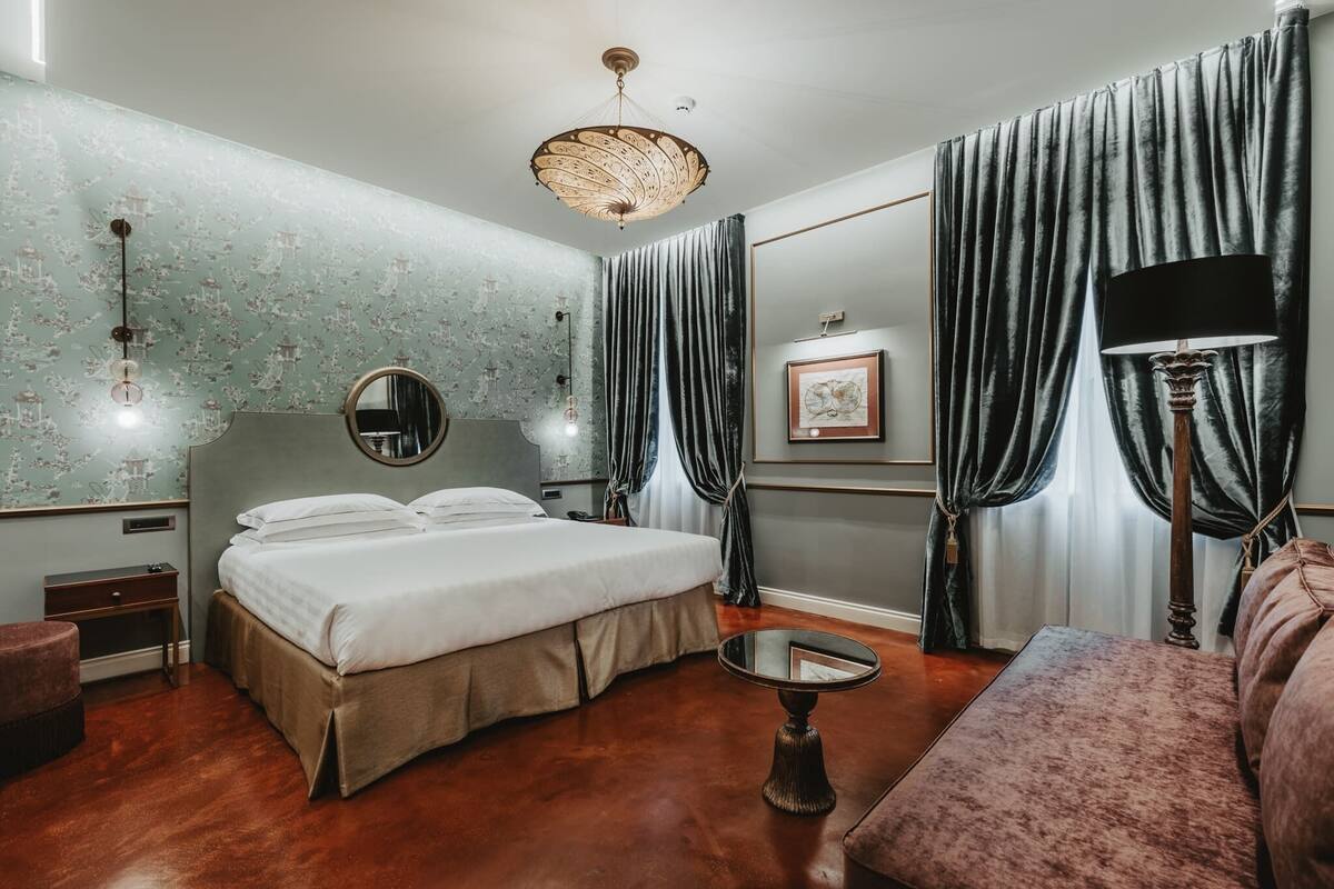 A bedroom with a large bed, a round mirror, a small table, a floor lamp, and a sofa.