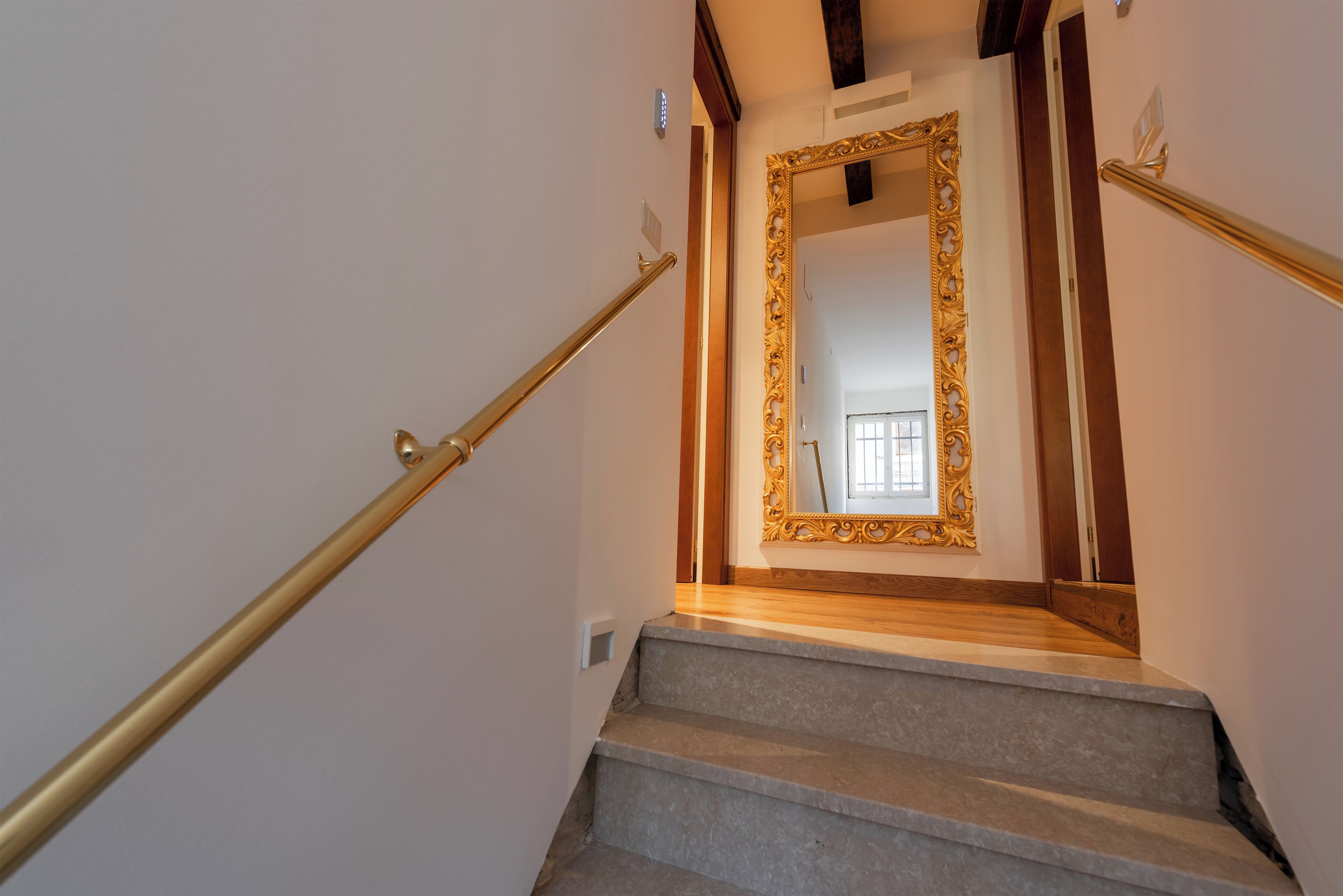 A staircase with a handrail and a large ornate mirror at the top.