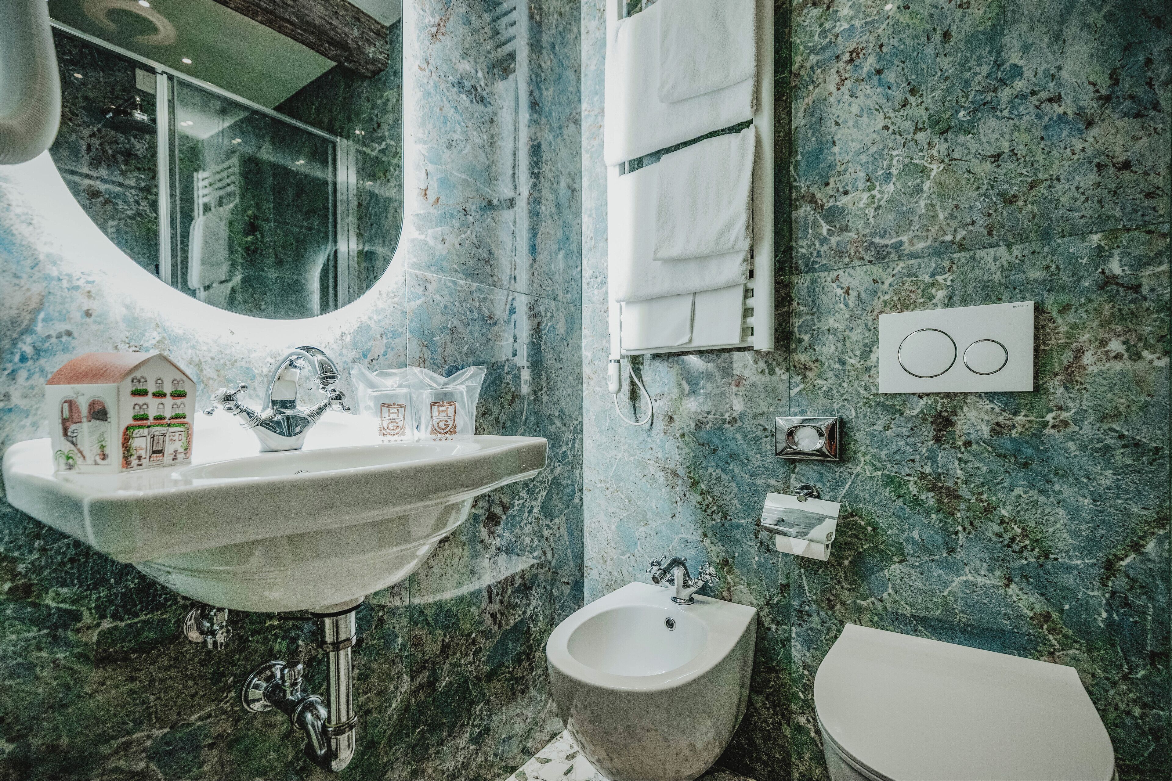 Un baño con lavamanos, bidé e inodoro, paredes de mármol y un espejo.