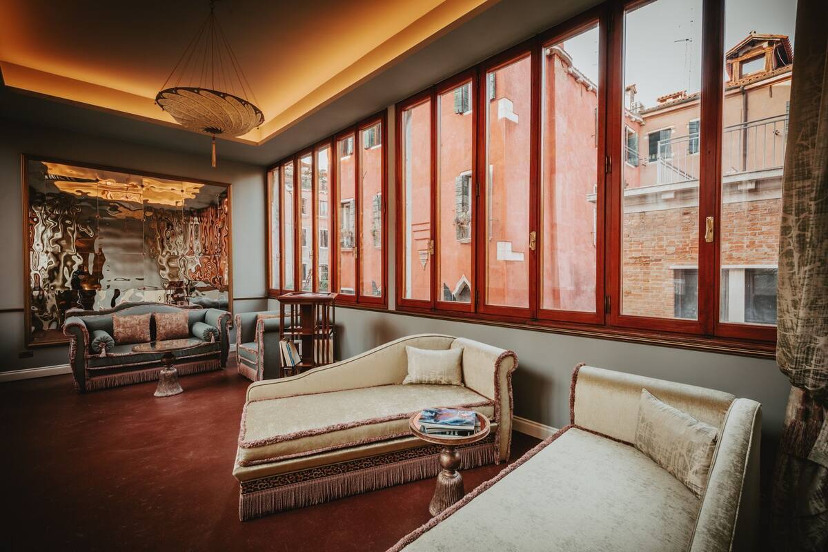 A cozy living room with a sofa, armchairs, and a coffee table. Large windows offer views of the cityscape.
