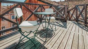 Una terraza de madera con sillas y una mesa de metal, con vistas a un paisaje urbano con tejados de teja.