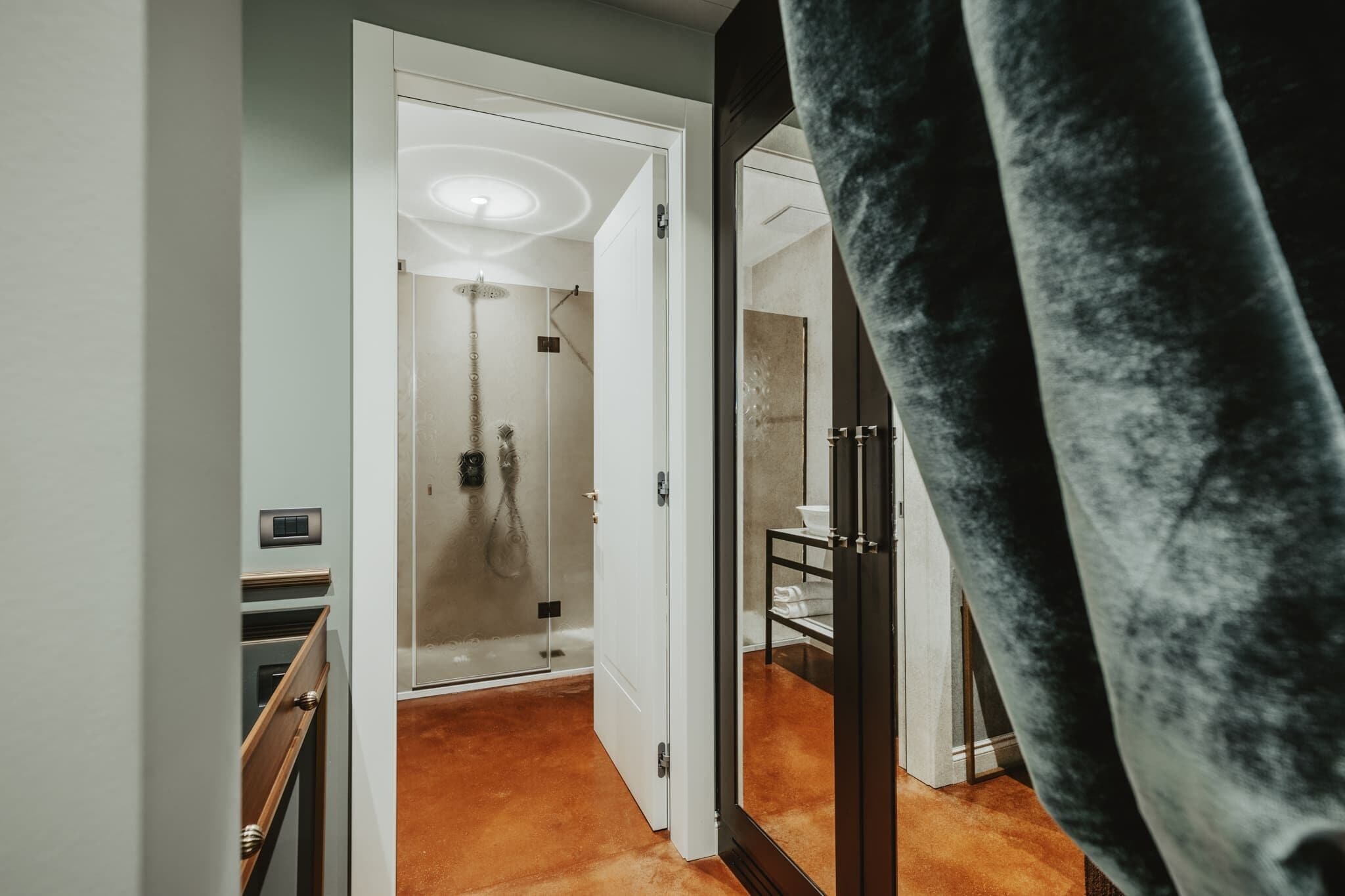 A modern hotel room with a glass shower, a wooden staircase, and a black velvet curtain.