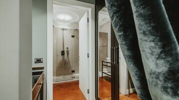 Una camera d'albergo moderna con doccia in vetro, una scala in legno e una tenda di velluto nero.
