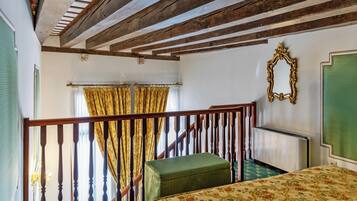 A room with a wooden staircase, a green upholstered bench, a bed with floral bedding, and a mirror on the wall.