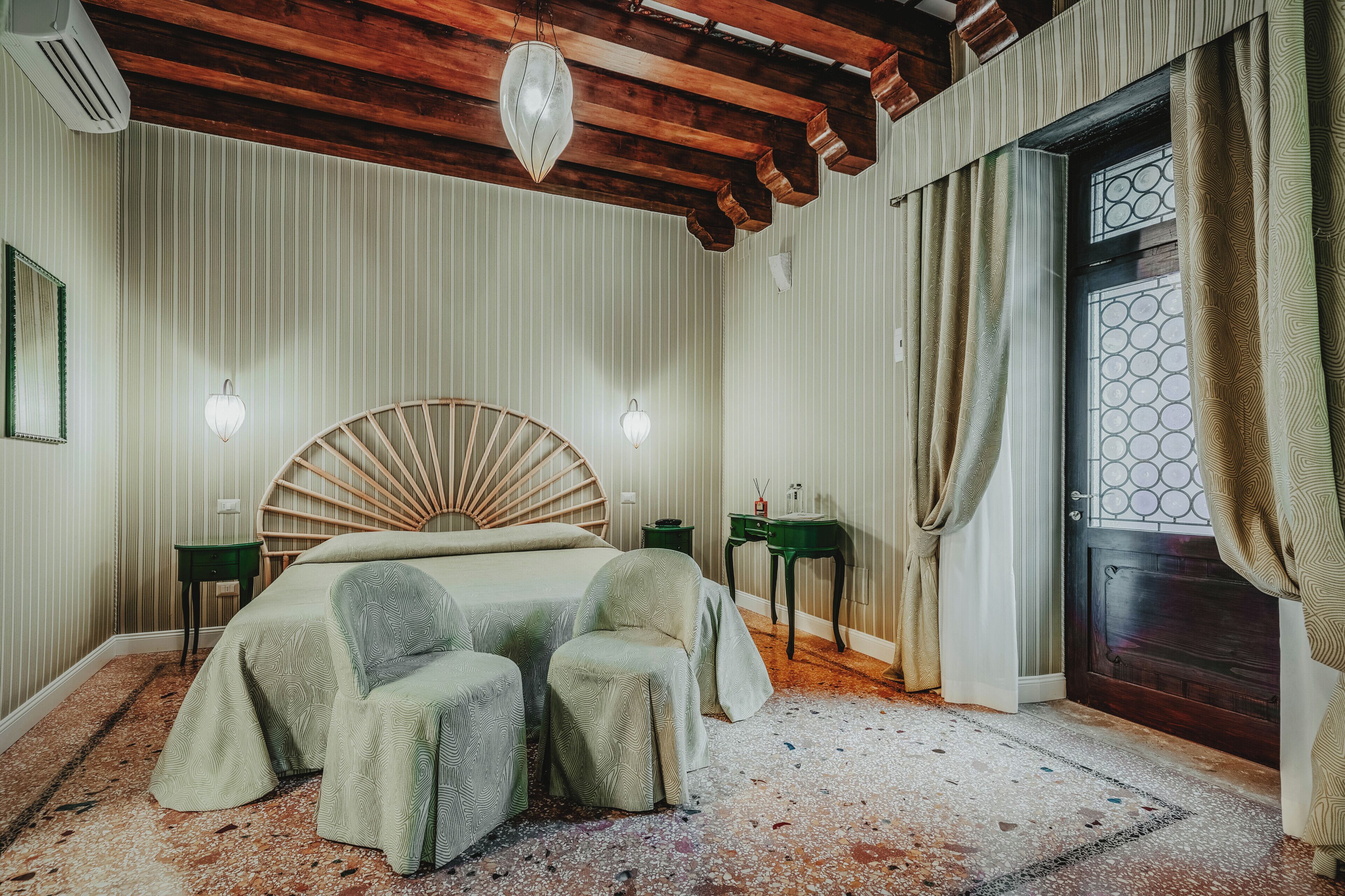 Un dormitorio con una cama grande, dos sillas, techo de madera, un espejo redondo en la pared y una puerta con diseño geométrico.