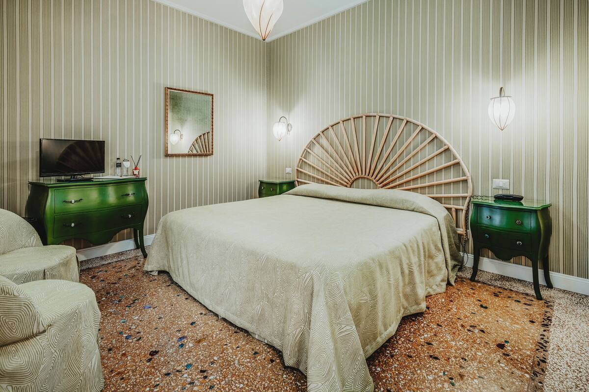 A hotel room with a large bed, a television, a green dresser, and a mirror.