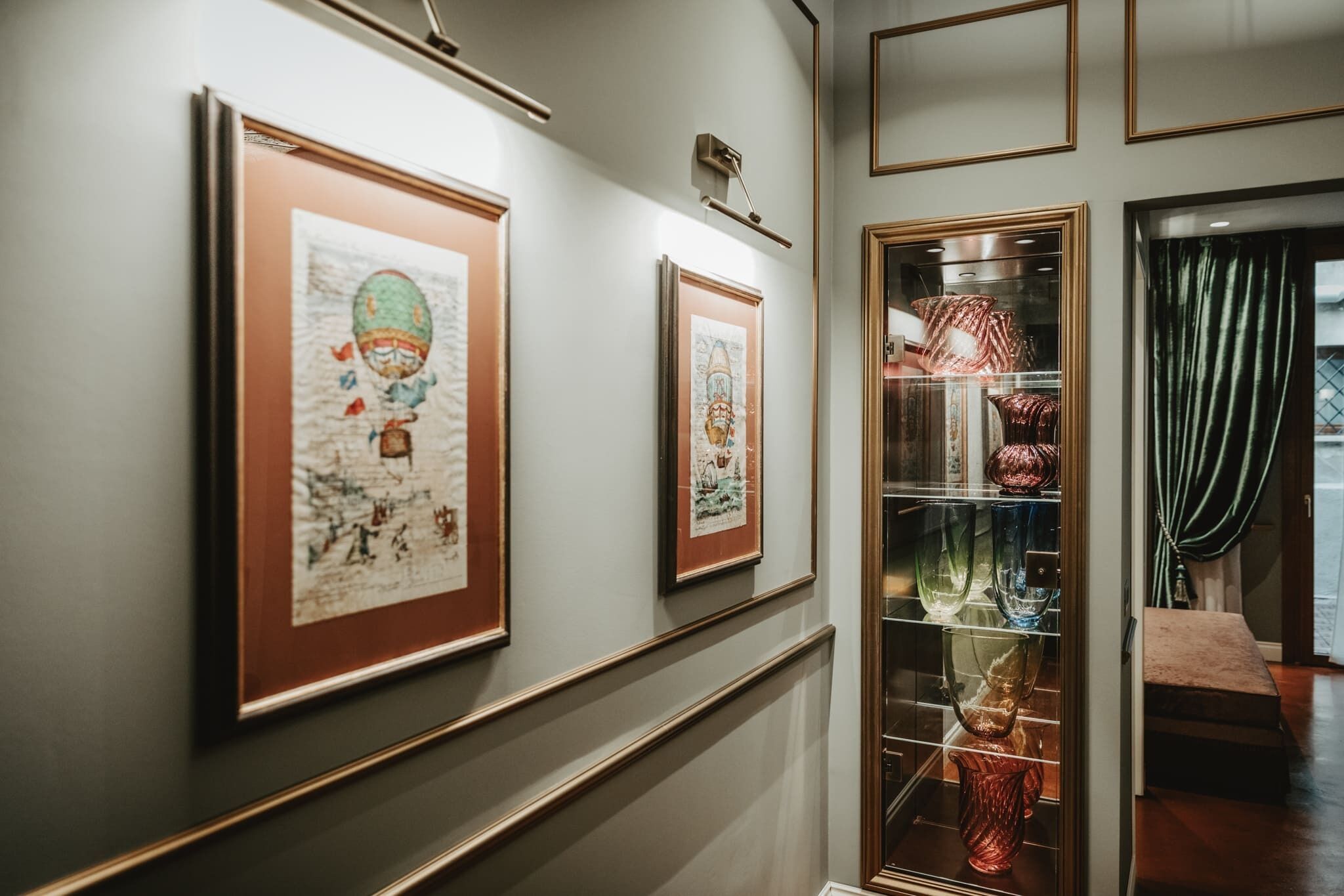 Un pasillo con obras enmarcadas en la pared y una vitrina de vidrio con objetos decorativos.