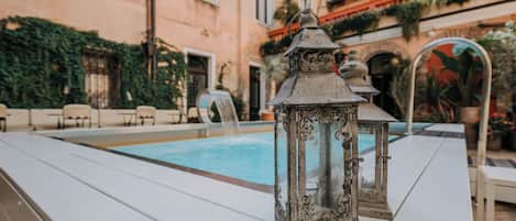 A poolside area with a white table, a decorative lantern, and a building with arched windows and greenery.