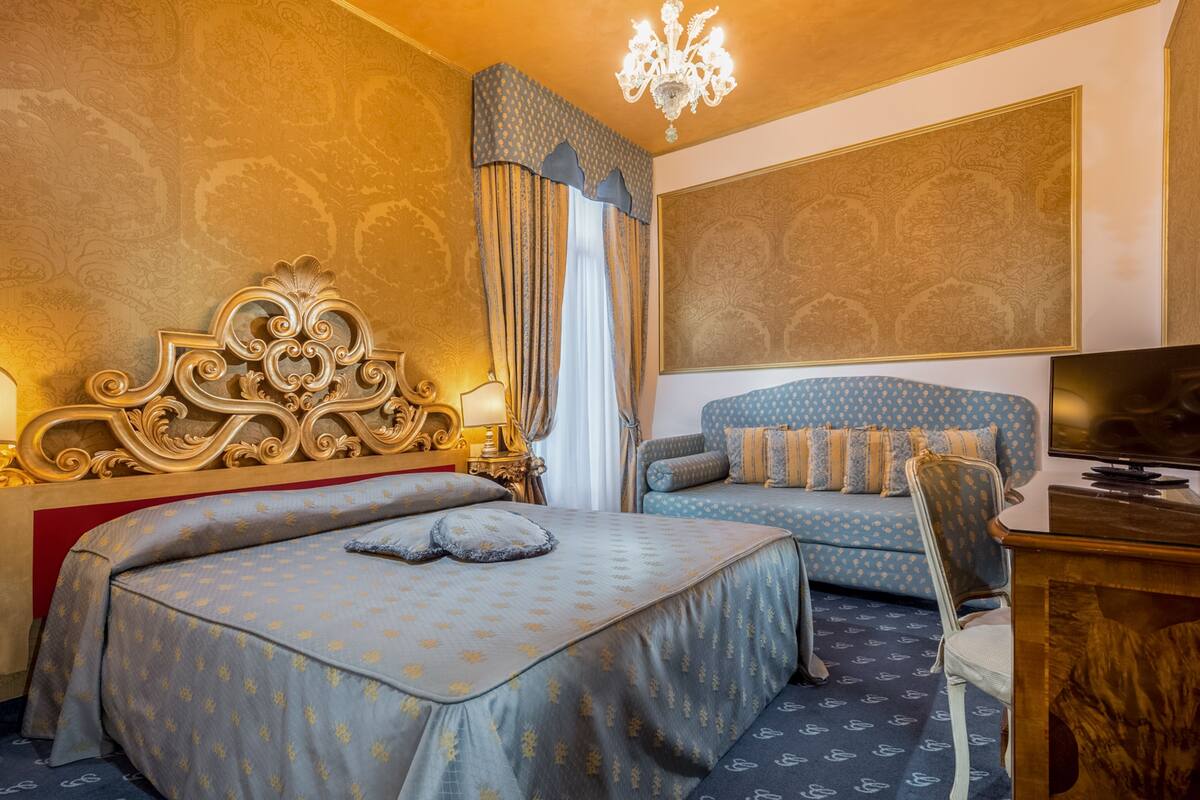 A hotel room with two beds, a TV, a desk, and a chandelier.