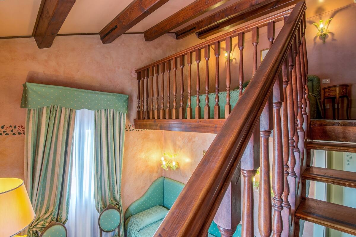 A wooden staircase with a green upholstered chair and a lamp near a window with striped curtains.