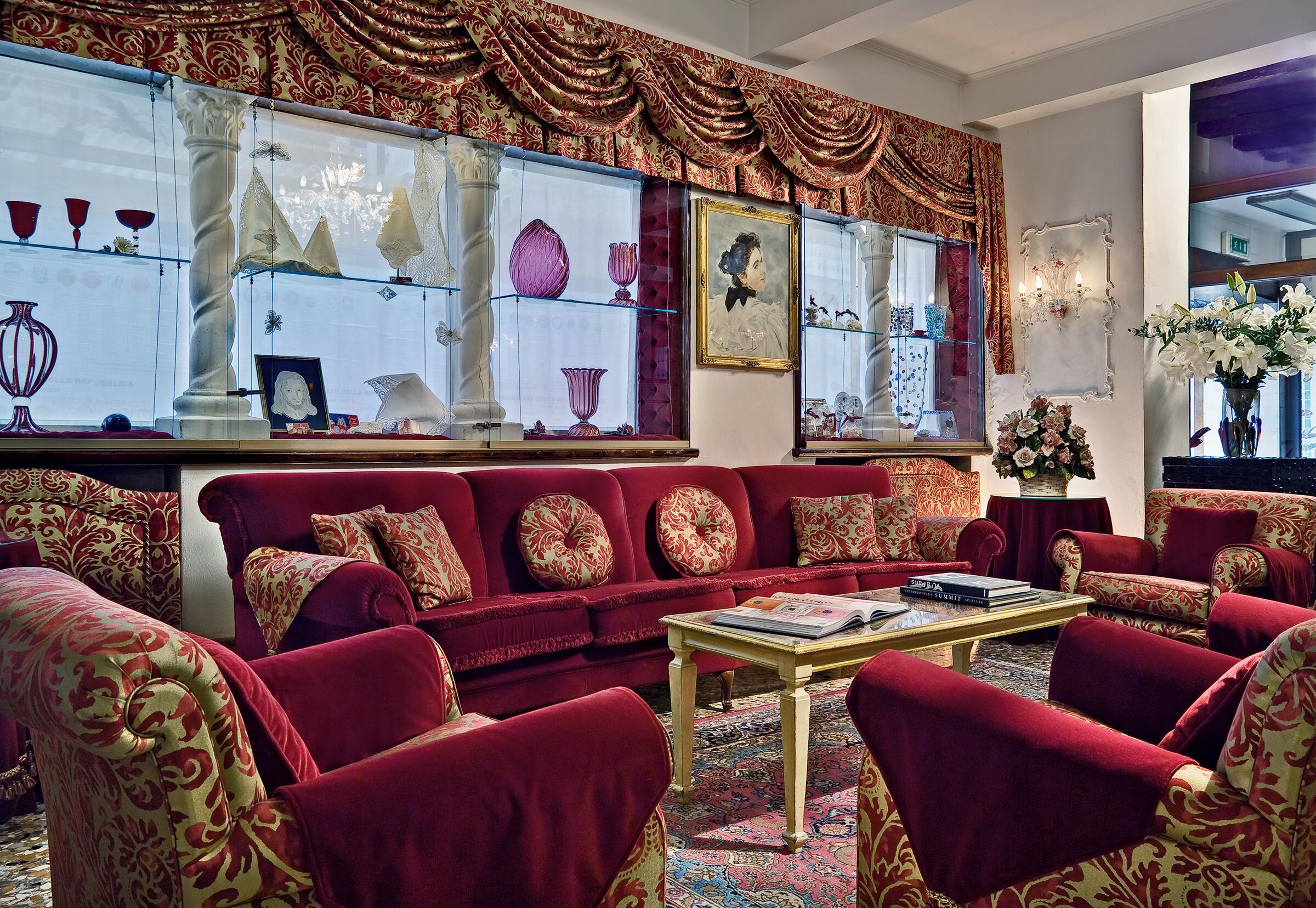 Un salon luxueux avec un ensemble de canapés rouges, une table basse et une vitrine en verre contenant des objets décoratifs.