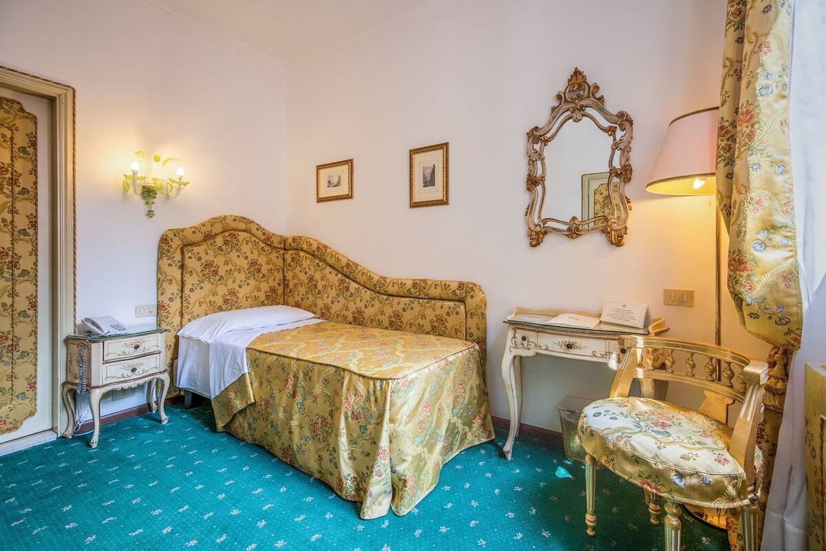 A bedroom with a bed, bedside table, lamp, chair, and a dresser.