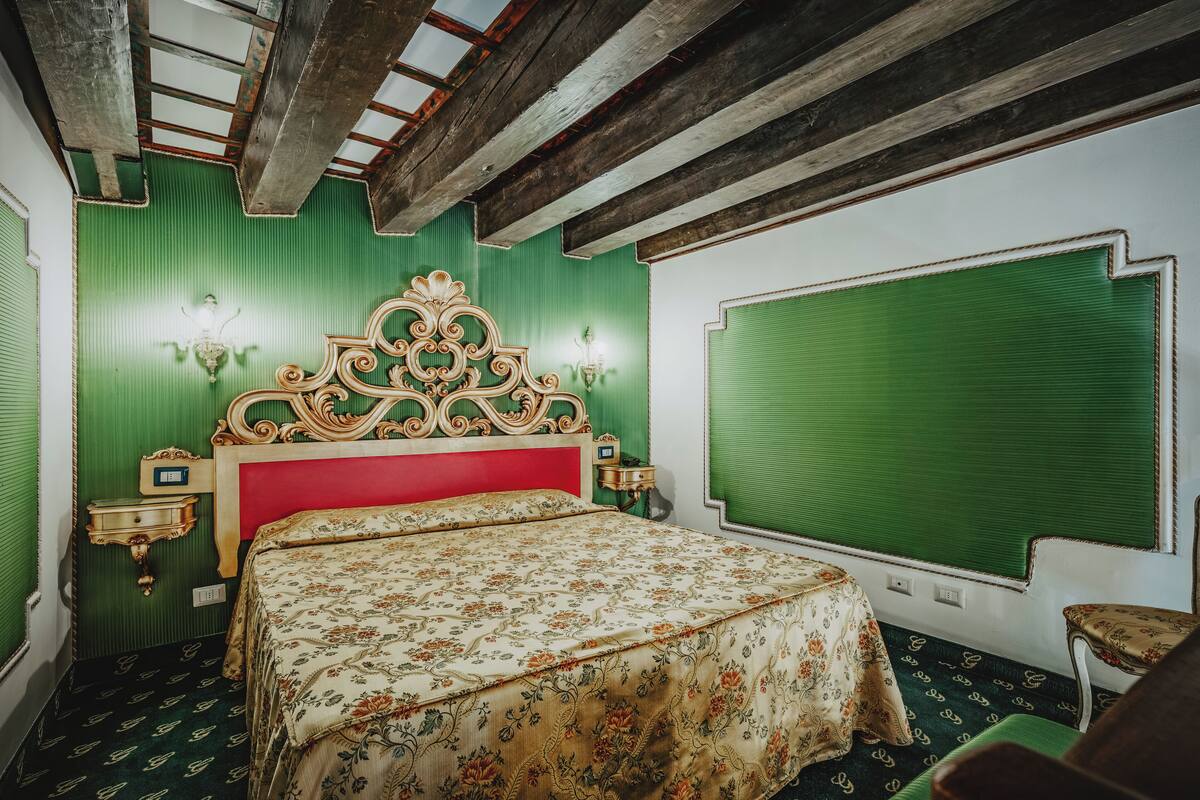 A room with a bed, green walls, a red headboard, and a green window blind.