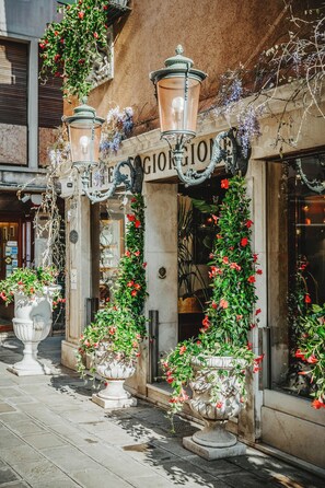 A building facade with a sign reading "GIOIA," adorned with hanging lanterns and potted plants with red flowers.