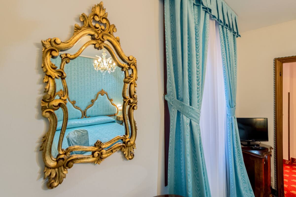 A room with a large ornate mirror, a blue patterned sofa, and a television on a wooden stand.