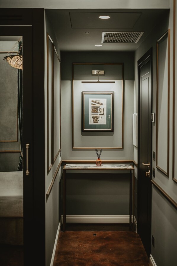 A narrow hallway with a framed picture on the wall, a small table with a vase, and a door on the right.