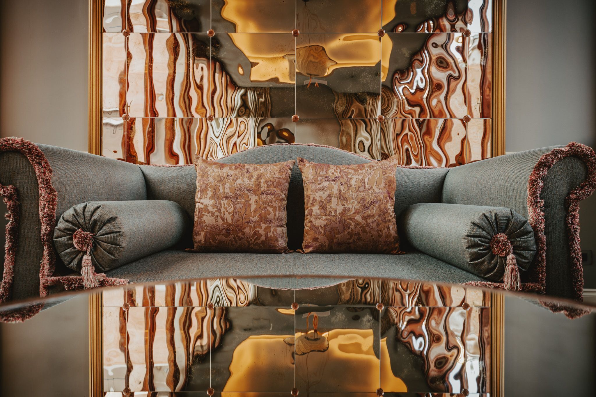A modern living room with a sofa, two patterned throw pillows, and a reflective wall.