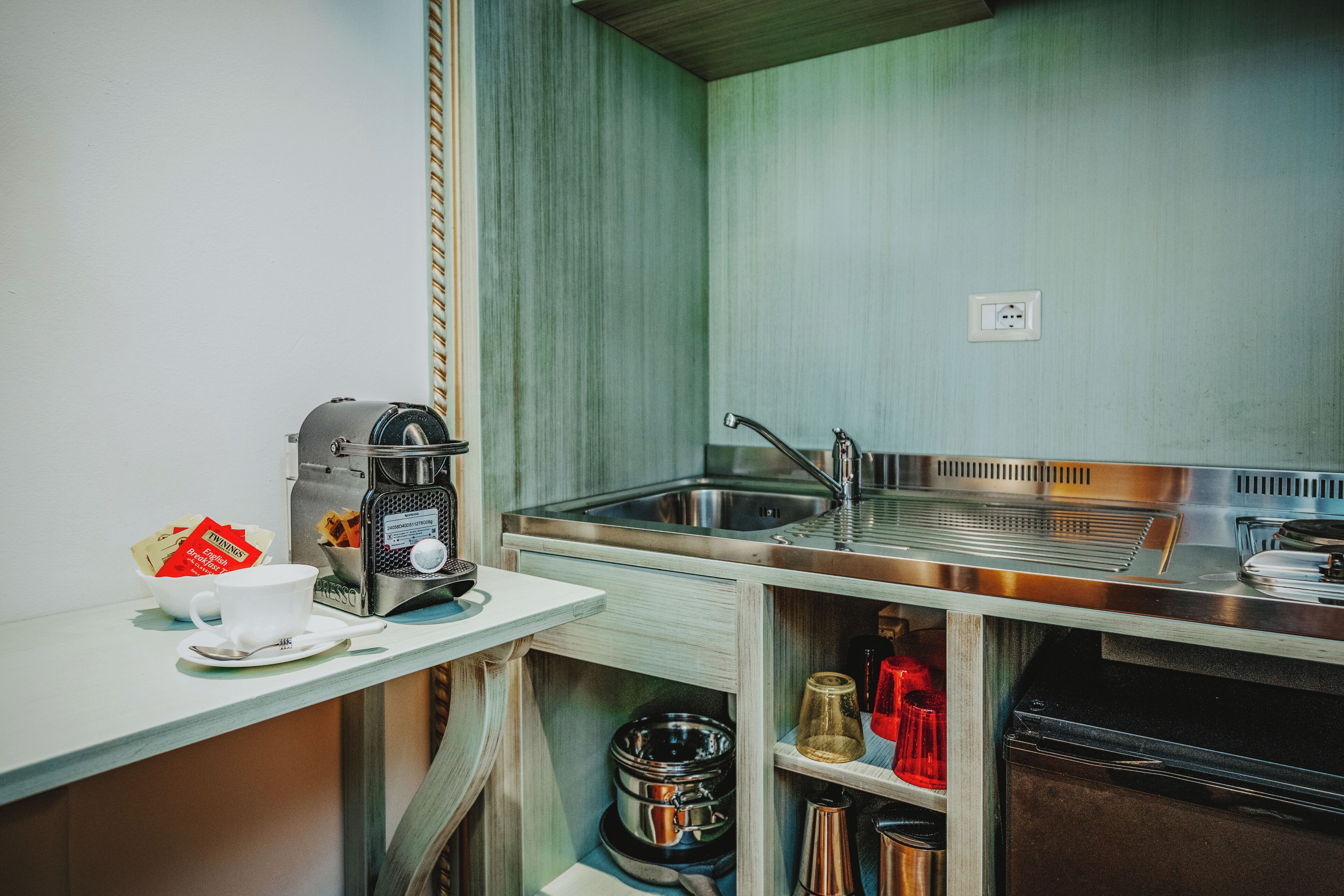 Una kitchenette compacta con cafetera, un lavamanos y un pequeño estante de almacenamiento.