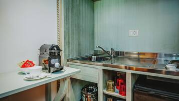 Una kitchenette compacta con cafetera, un lavamanos y un pequeño estante de almacenamiento.