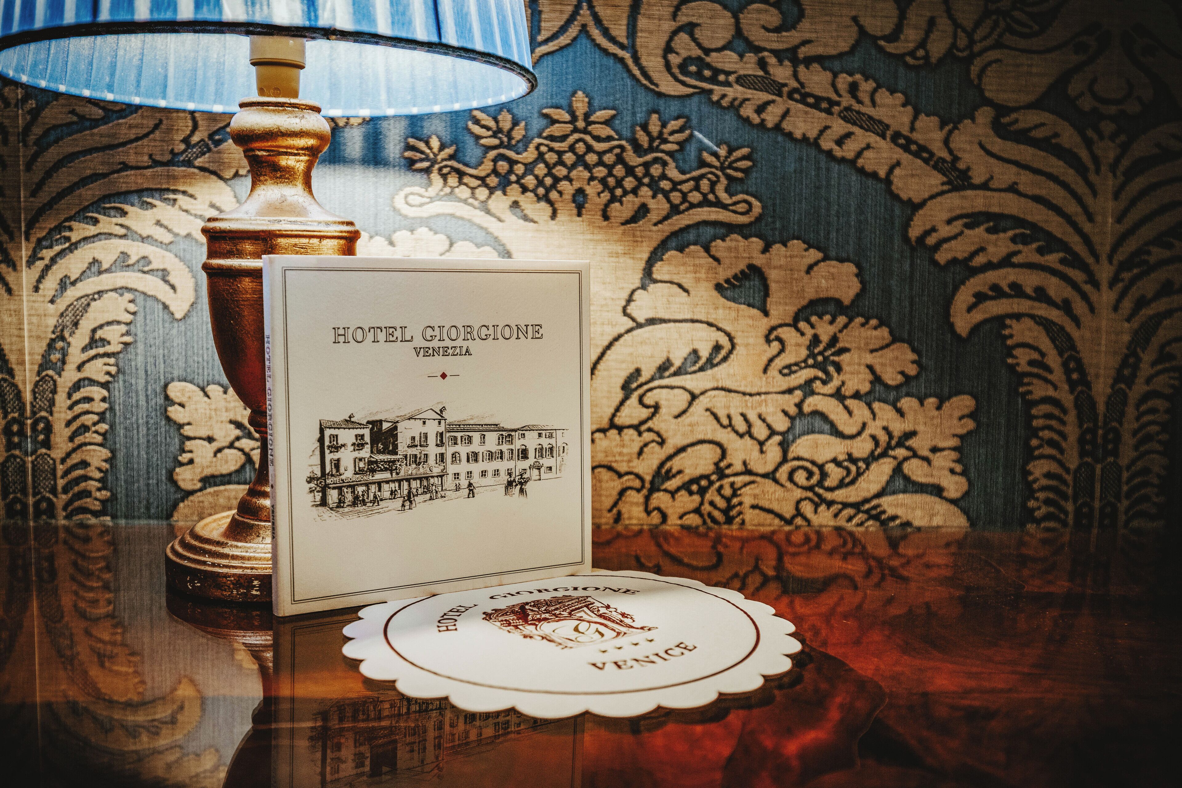 A hotel brochure with a building illustration, a lamp, and a coaster with the hotel's name.