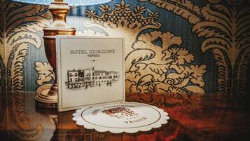 A hotel brochure with a building illustration, a lamp, and a coaster with the hotel's name.