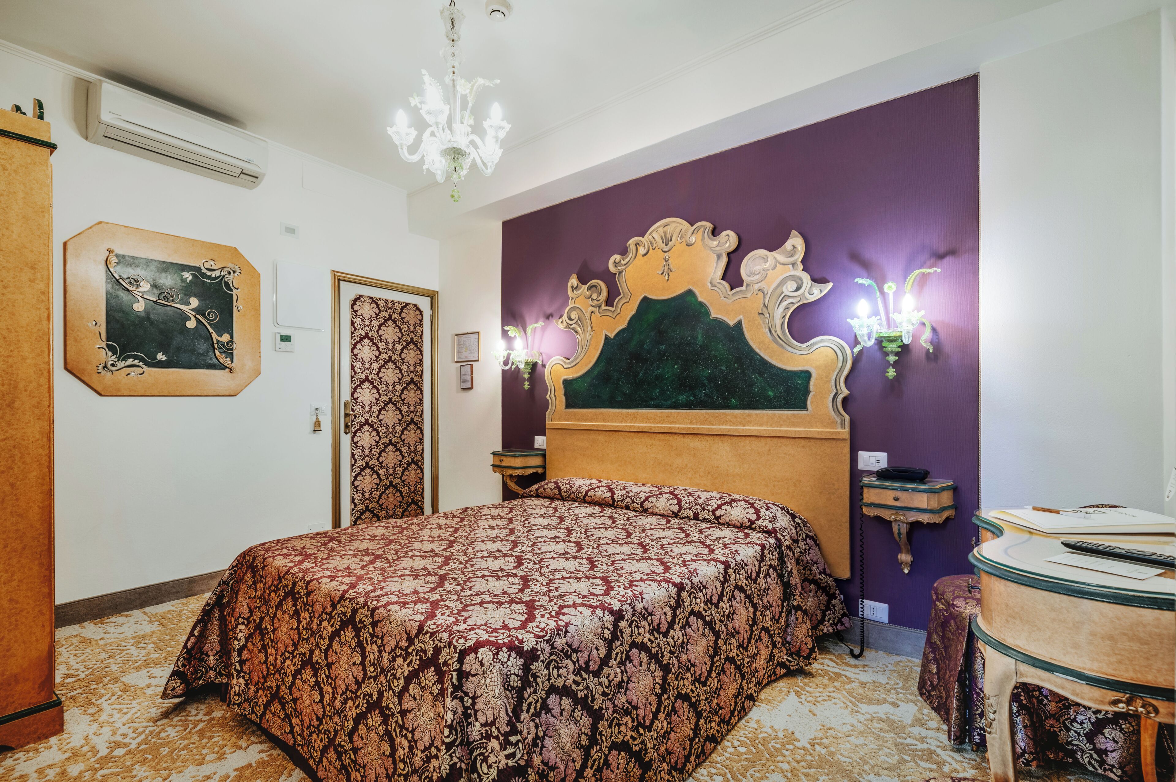 Un dormitorio con una cama grande, una araña, una pared de acento morada y una mesita de noche pequeña.