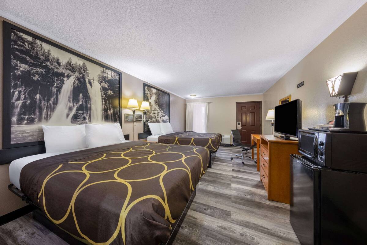 Una camera d'albergo con due letti, una televisione, un frigorifero e una scrivania con lampada.