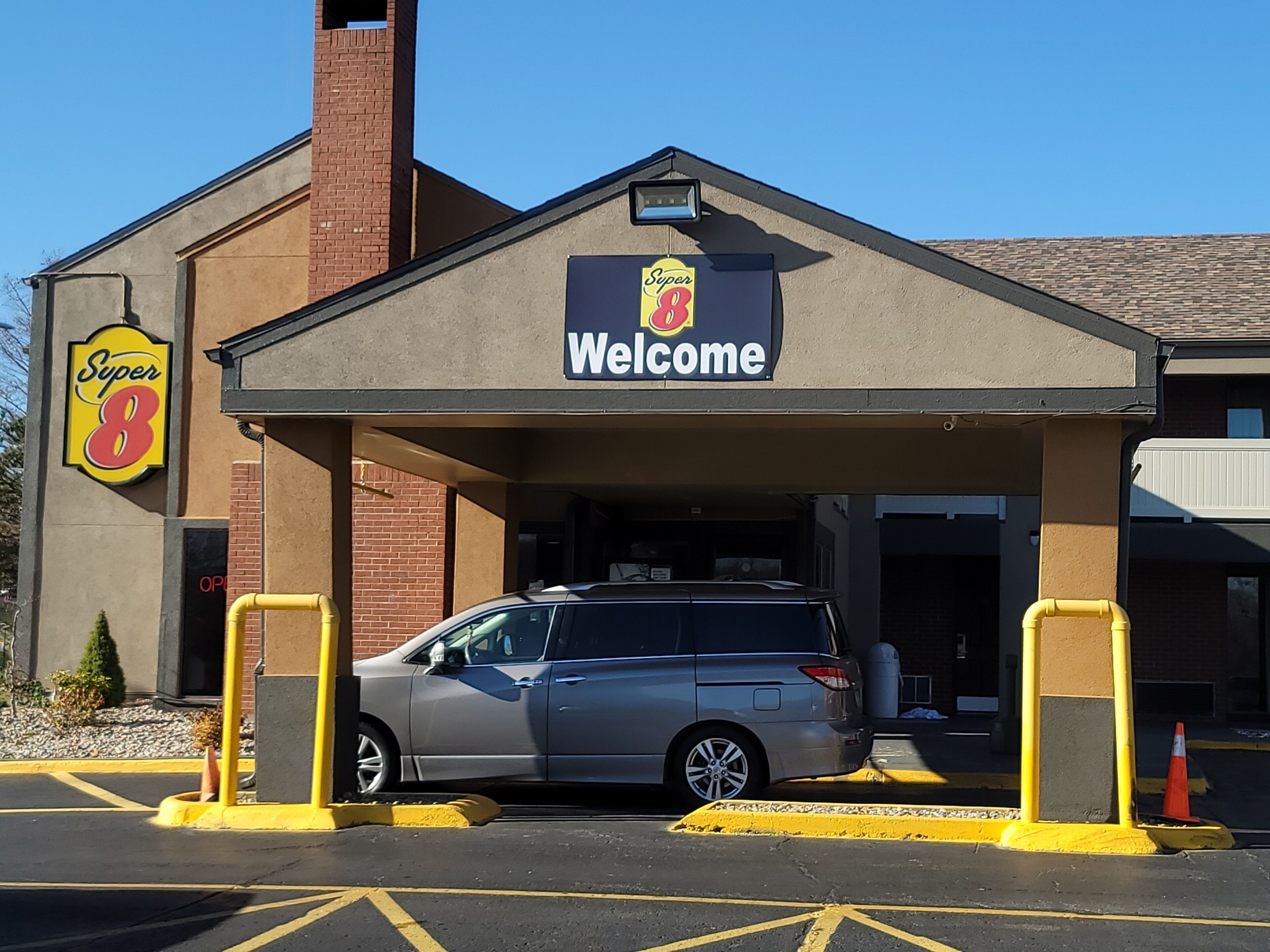 A Super 8 hotel entrance with a covered parking area and a parked car.