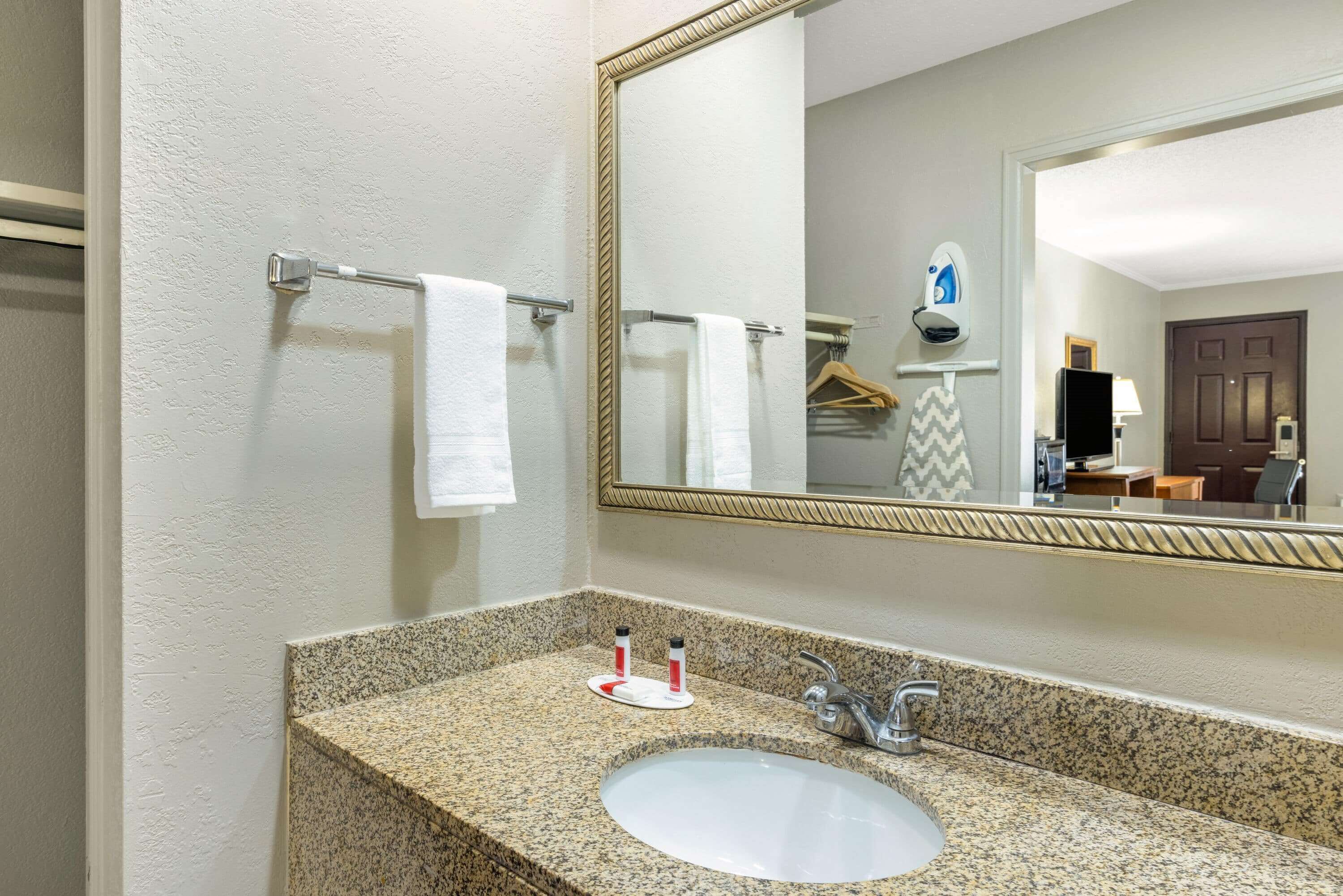 A bathroom with a granite countertop sink, a mirror, and two towels hanging on a towel rack.