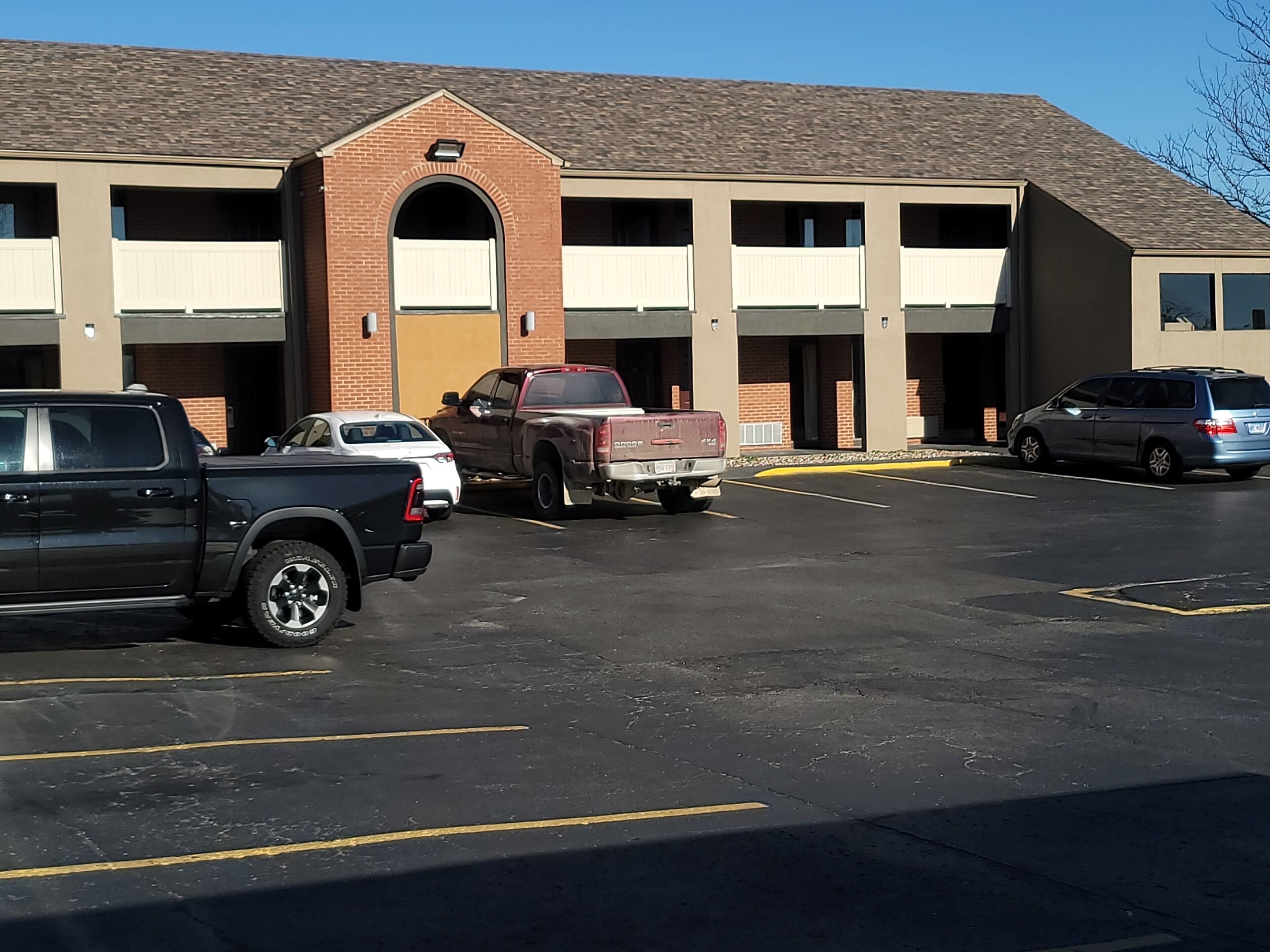 A parking lot with several vehicles, a building with a brick facade and multiple garage doors, and a clear sky.