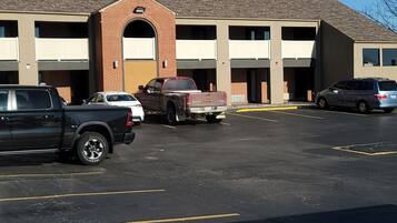 A parking lot with several vehicles, a building with a brick facade and multiple garage doors, and a clear sky.