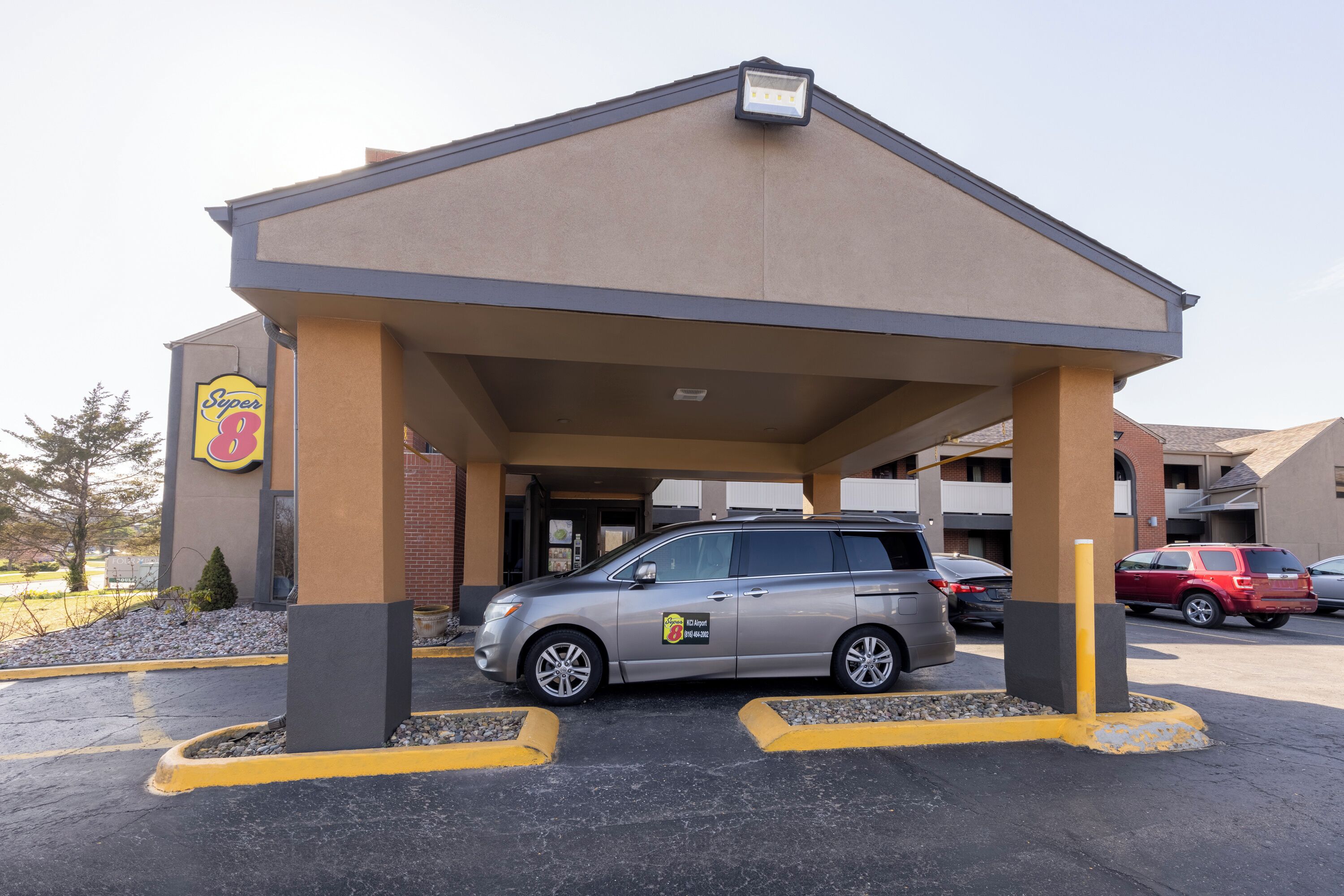 A parking area with a covered entrance to a building, a parked SUV, and a Super 8 sign.