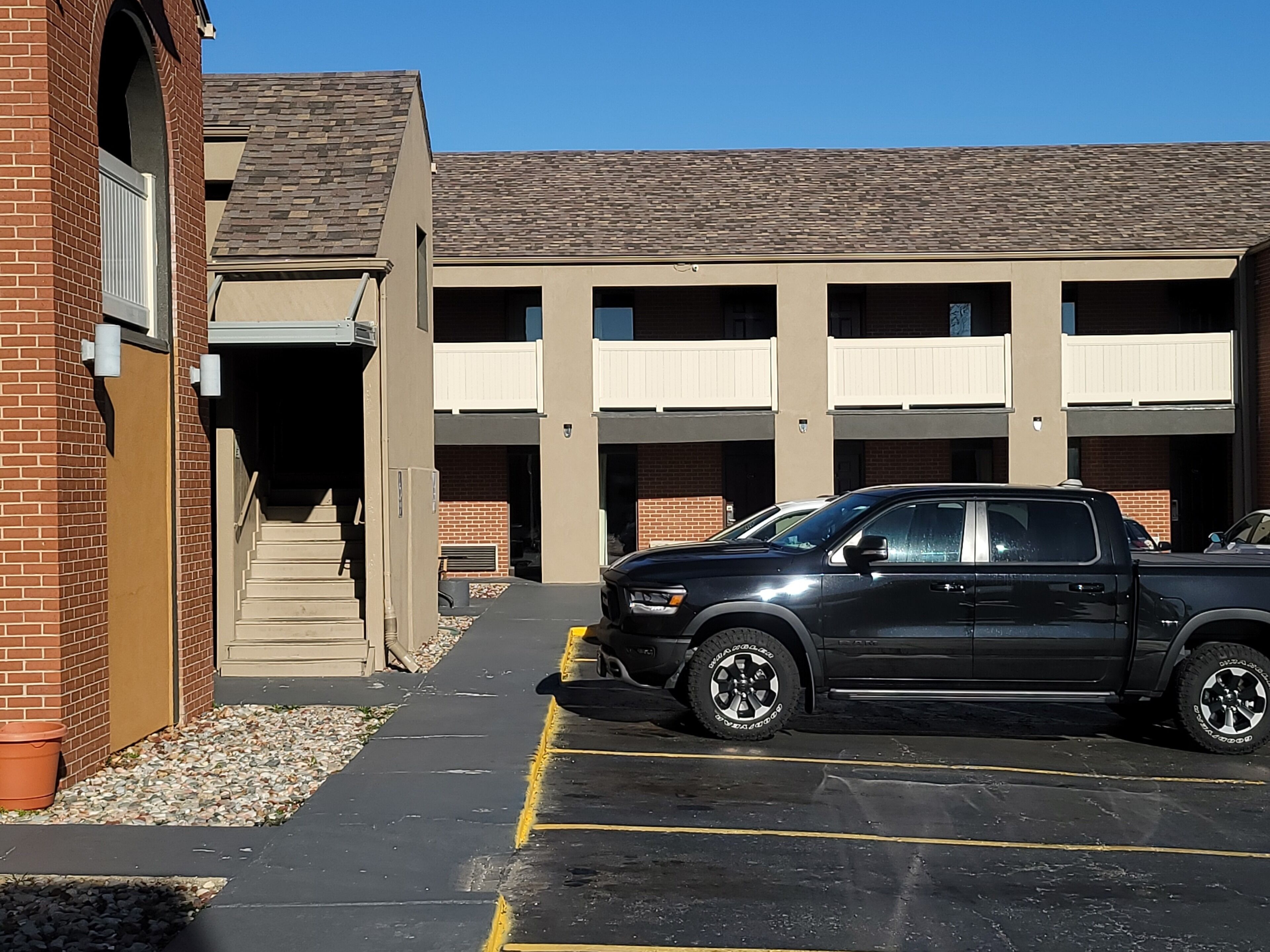 A parking area with a black pickup truck parked in front of a building with multiple balconies.