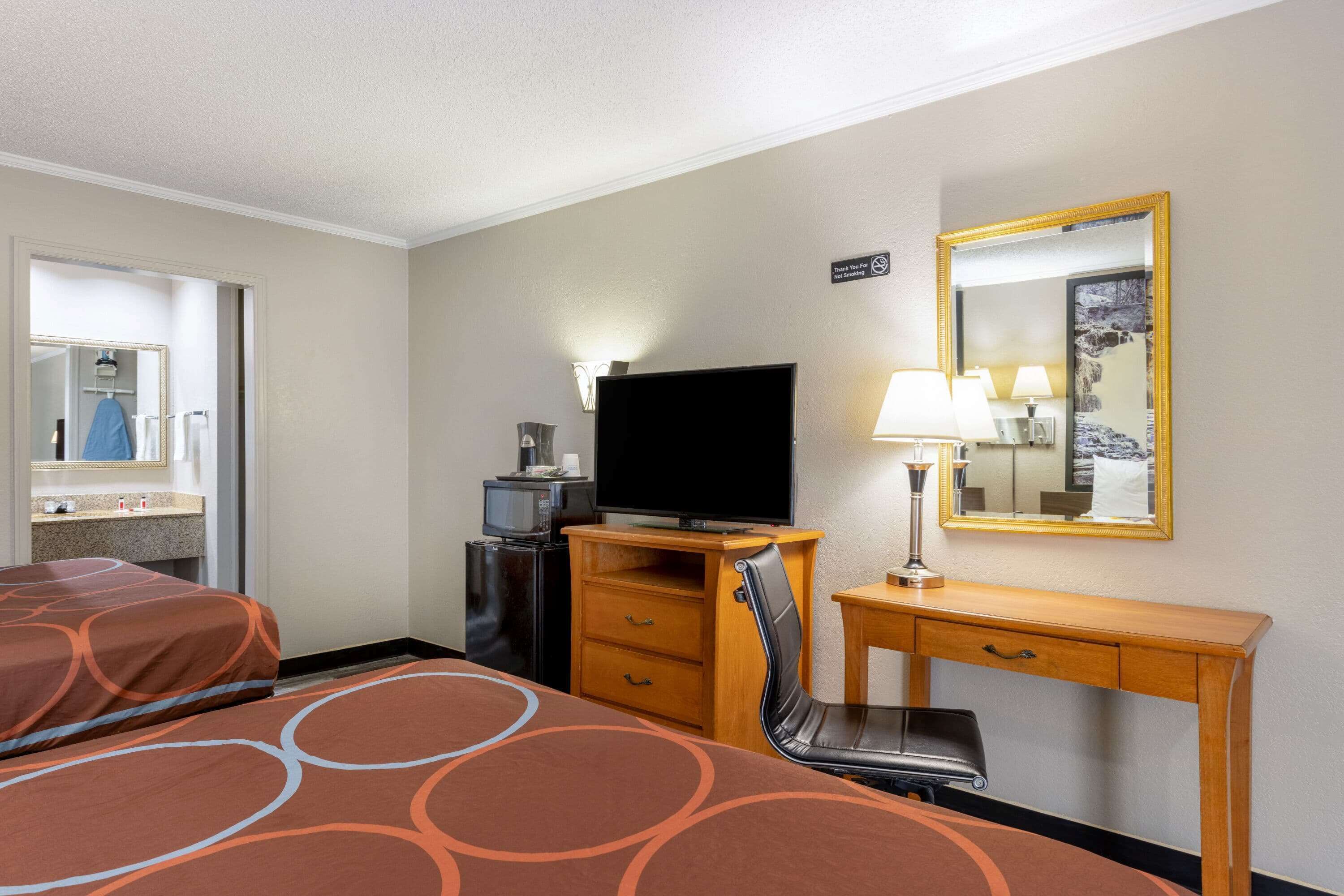 A hotel room with two beds, a desk with a chair, a television, a mirror, and a small table with lamps.