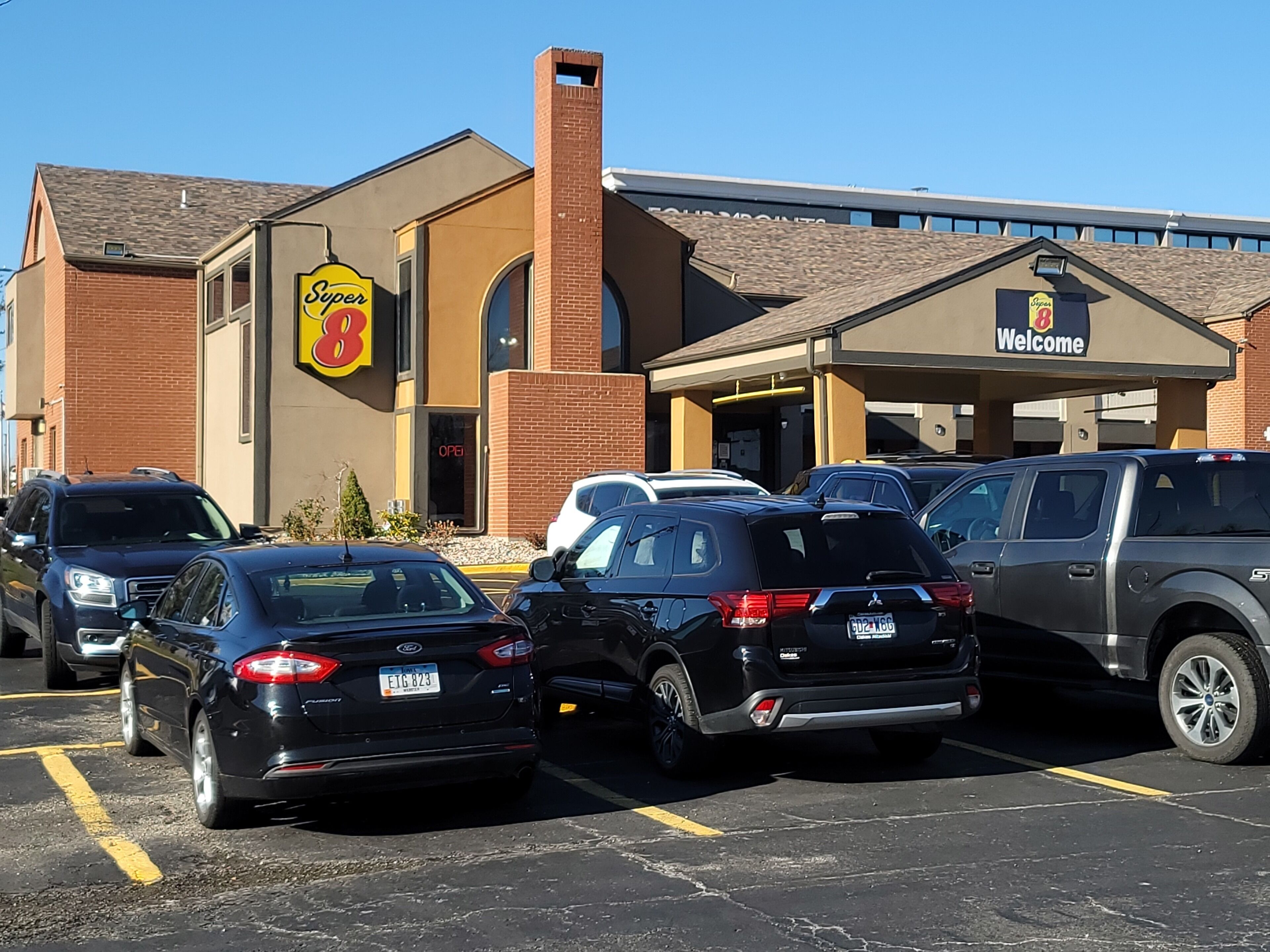 A Super 8 hotel with a brick facade, a large parking lot, and several parked cars.