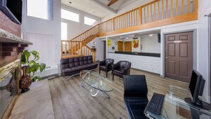 A spacious living area with a fireplace, leather sofas, a glass coffee table, and a computer desk.