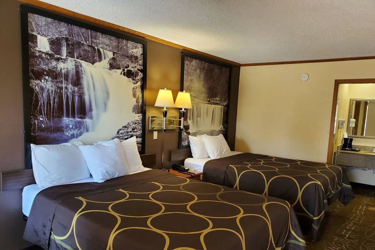 Una camera d'albergo con due letti, un grande quadro raffigurante una cascata, una lampada da comodino e uno specchio.