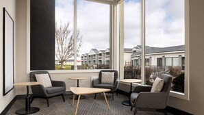 A modern hotel room with a large window, a gray carpet, and a seating area with two armchairs and two small round tables. - Holiday Inn Ontario by IHG (Ontario)
