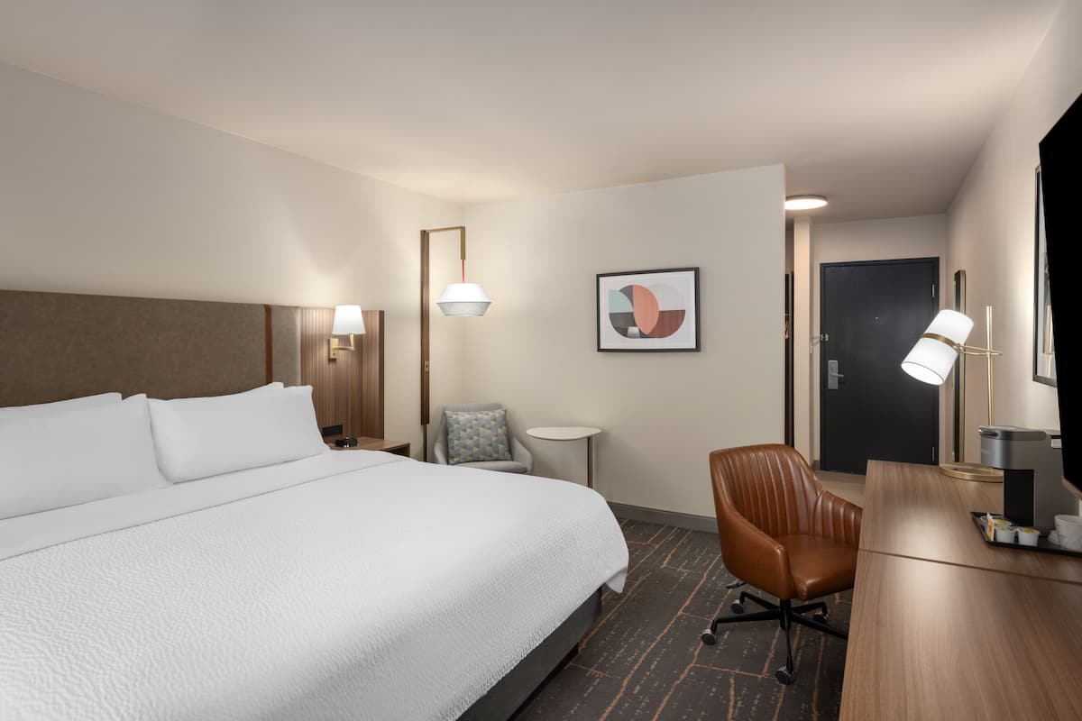 A hotel room with a large bed, a desk, a chair, and a small table.