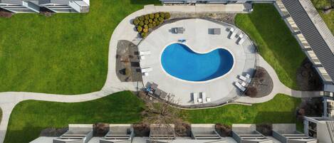 An aerial view of a residential area with a swimming pool, a landscaped garden, and a building with a sloped roof.