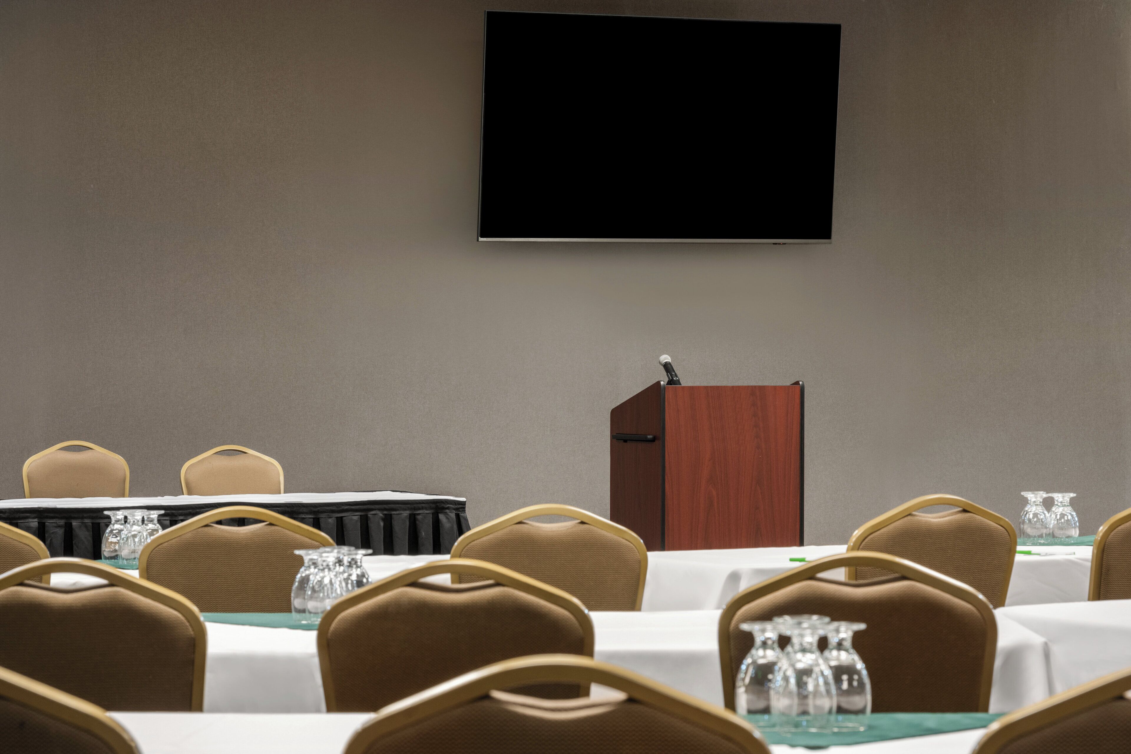 A conference room with a large screen, a podium, and multiple tables with chairs.