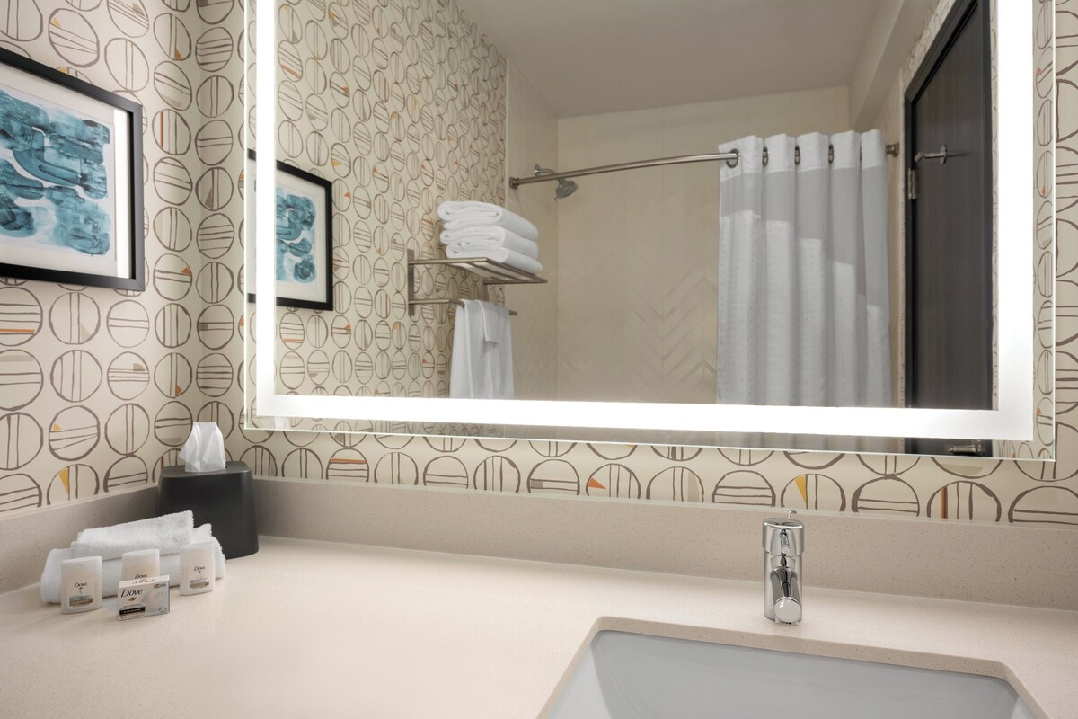 A bathroom with a large mirror, a sink, a towel rack, and a shower curtain.