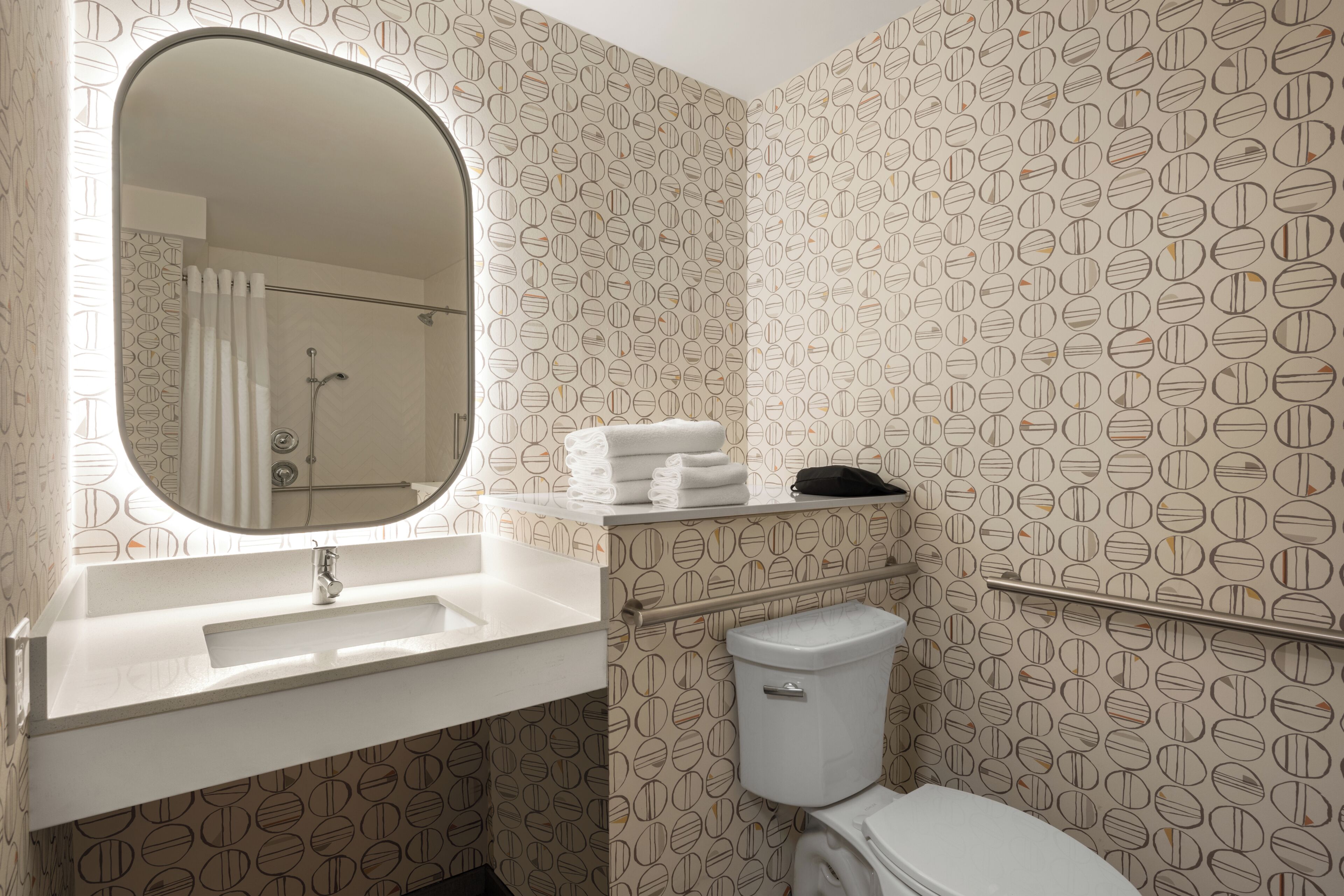 Un baño con espejo redondo, lavamanos blanco y retrete.